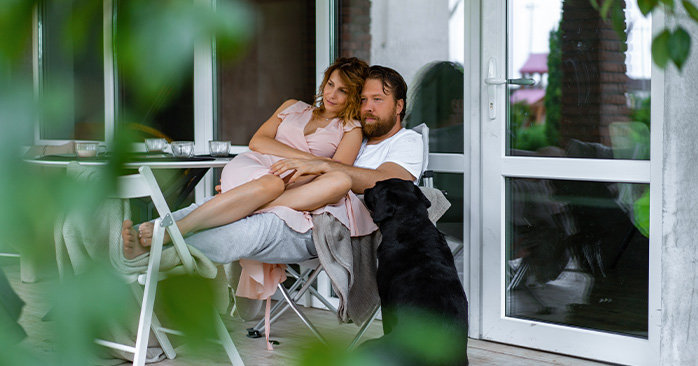 Couple relaxing, cuddling on porch with dog starring up at them.